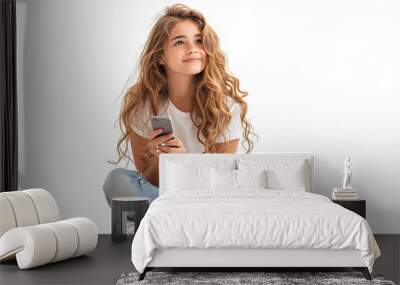 Happy young girl sitting on the floor, holding smartphone in hands and looking away, on isolated transparent background Wall mural