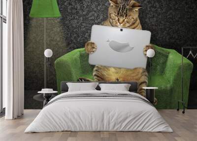 The cat reads a laptop on the green couch near a floor lamp in the living room. Wall mural