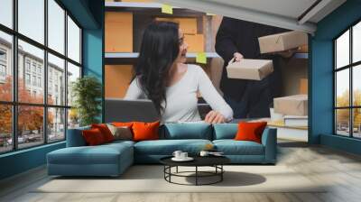 SME entrepreneur man is looking and holding a parcel while his partner looking at the box in warehouse. Concept of online delivery working at home. Shipping package. Focus at box Wall mural