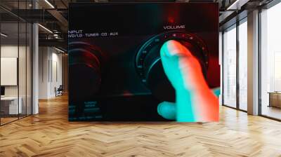 A woman's hand turns on and increases the volume of music on the amplifier. Colorful neon light. Macro view. Close-up of volume controls panel. Audio Receiver Control Panel. Control panel by sound amp Wall mural