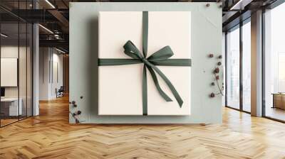 Beige gift box wrapped with a dark green ribbon, set on a light green background with scattered winter elements like pine and dried berries. minimalistic Birthday invitation card.. Wall mural