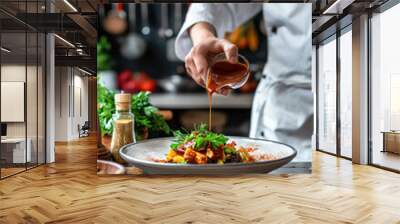 Chef pouring sauce over a plated dish in a professional kitchen.. Wall mural