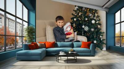 boy sitting with a toy in his hands against the background of a Christmas tree Wall mural