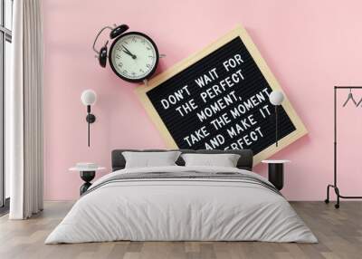 Don't wait for the perfect moment, take the moment and make it perfect. Motivational quote on letter board, black alarm clock on pink background. Concept inspirational quote of the day Wall mural