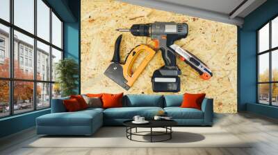 Drill, construction knife and construction stapler on a wooden background Wall mural