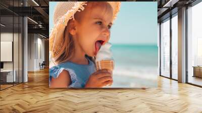 Cute little girl in a straw hat eating soft melted butter ice cream in a waffle glass on the background of the sea Wall mural