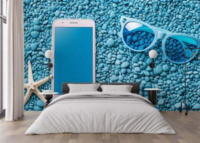 Flat lay of blue blank phone screen, sunglasses and starfish on sand with blue sand background. Wall mural