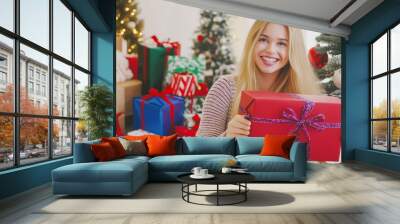 Happy romantic woman standing against Christmas tree background. Cheerful lady surprised of the present after the opening in the gift box. Merry Christmas and Happy Holidays Wall mural