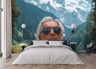 A stylish elderly man in aviator sunglasses drives a retro convertible along a scenic mountain road with snow-capped peaks in the background Wall mural