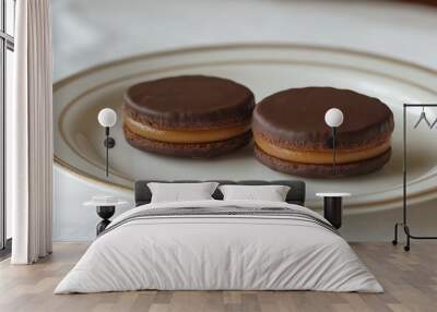 A traditional Argentine alfajor featuring two round cookies filled with dulce de leche and coated in chocolate, displayed on a white plate Wall mural