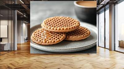 A traditional Dutch stroopwafel featuring two thin waffle cookies with caramel syrup filling on a white plate beside a cup of coffee Wall mural