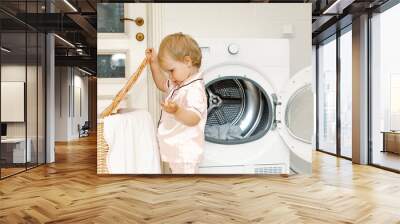 Child girl little helper in laundry room near washing machine and dirty clothes in washing basket. washing and cleaning concept. daily routine. Copy space Wall mural