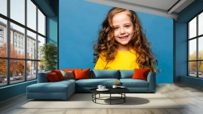 Close-up portrait of nice-looking pretty cute lovely attractive cheerful cheery content long-haired little girl in yellow t-shirt isolated over vibrant blue color background Wall mural