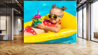 Cute child, little girl near the swimming pool in sunglasses drinks a cocktail. Summer vacation concept. Wall mural