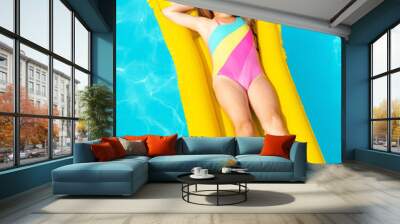 Cute little girl lying on inflatable mattress in swimming pool with blue water on warm summer day on tropical vacations. Summertime activities concept. Cute little girl sunbathing on air mattress Wall mural