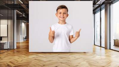 Happy smiling satisfied caucasian boy shows thumbs up looking at camera, portrait. attractive smiling boy in white casual shirt posing on white background. childhood, human emotions, lifestyle Wall mural