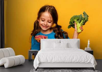 Hungry little child girl is hard to choose a donut or broccoli on yellow background. Unhealthy vs healthy food. Concept of choice. junk food Wall mural