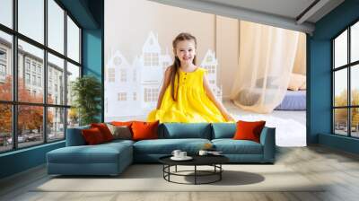 Little cute girl in yellow dress plays in the bright children's room. Funny cute little girl having fun in the children's room. Wall mural