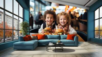 Two happy little American children boy and girl sit by the table and eat delicious hamburgers and fries. unhealthy food Childhood concepts and eating. Wall mural