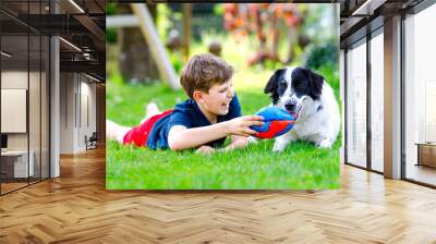 Active kid boy playing with family dog in garden. Laughing school child having fun with dog, with running and playing with ball. Happy family outdoors. Friendship between animal and kids Wall mural