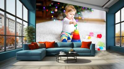 Adorable cute beautiful little baby girl playing with educational toys at home or nursery. Happy healthy child having fun with colorful wooden rainboy toy pyramid. Kid learning different skills. Wall mural