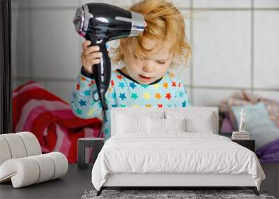 Cute little toddler girl making hairs with hair dryer. Adorable healthy baby child with wet hairs after taking bath. Beautiful girl having fun with toy Wall mural