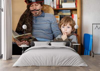 Father reading pirate book to his 4 years son, indoors Wall mural