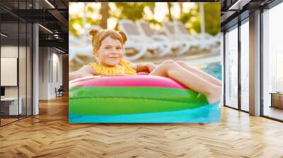 Happy little girl with inflatable toy ring float in swimming pool. Little preschool child learning to swim and dive in outdoor pool of hotel resort. Healthy sport activity and fun for children. Wall mural