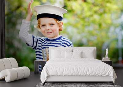 Happy little kid boy in sailor capitain hat and uniform playing with sailor boat ship. Smiling preschool child dreaming and having fun. Education, profession, dream concept Wall mural