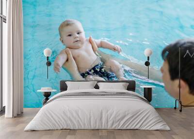 Happy middle-aged father swimming with cute adorable baby in swimming pool. Smiling dad and little child, newborn girl having fun together. Active family spending leisure and time in spa hotel Wall mural