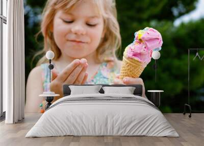 Happy preschool girl eating colorful ice cream in waffle cone on sunny summer day. Little toddler child eat icecream dessert. Sweet food on hot warm summertime days. Bright light, colorful ice-cream Wall mural