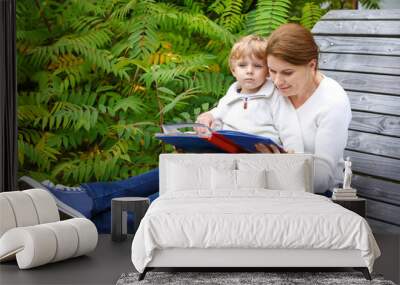 Little boy and his mother sitting on bench in park and reading b Wall mural