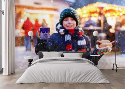 Little cute kid boy eating German sausage and drinking hot children punch on Christmas market. Happy child on traditional family market in Germany. Laughing boy in colorful winter clothes Wall mural