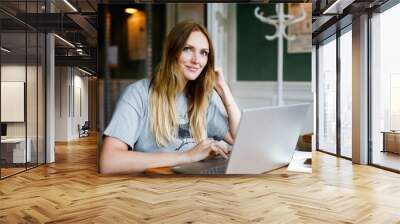 Portrait of young woman using technology of smartphone and looking at laptop. Young woman freelancer using laptop computer working in restaurant or hipster indoor cafe with coffee. Home office concept Wall mural