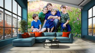 Summer portrait of parents with three children. Mother, father, two kids brothers boys and little cute toddler sister girl having fun together on flower meadow. Happy family of five Wall mural