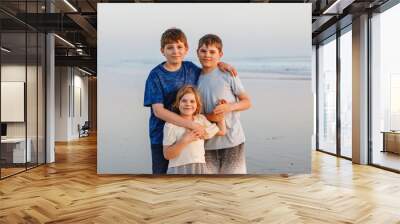 Three kids standing on beach at sunset. happy family, two school boys and one little preschool girl. Siblings having fun. Wall mural