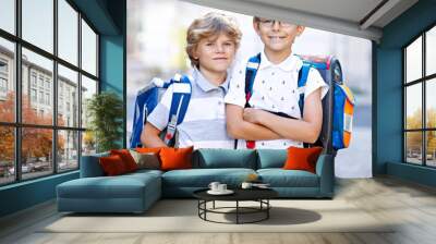 Two little kid boys with backpack or satchel. Schoolkids on the way to school. Healthy adorable children, brothers and best friends outdoors on the street leaving home. Back to school. Happy siblings. Wall mural