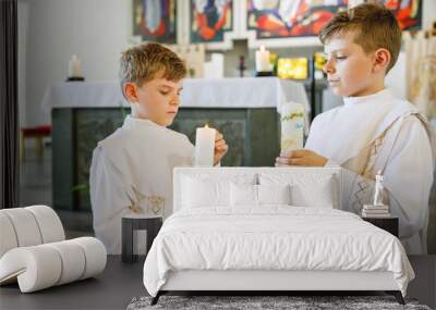 Two little kids boys receiving his first holy communion. Happy children holding Christening candle. Tradition in catholic curch. Kids in a church near altar. Siblings, brothers in white gowns. Wall mural