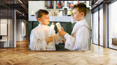 Two little kids boys receiving his first holy communion. Happy children holding Christening candle. Tradition in catholic curch. Kids in a church near altar. Siblings, brothers in white gowns. Wall mural