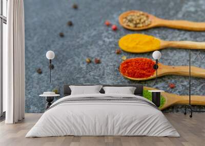 Spices lie in wooden spoons on a black background, top view, soft focus. Spices and seasonings for cooking in the composition on the table. Wall mural