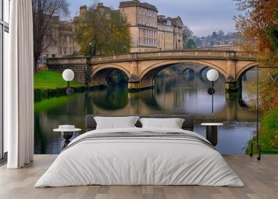 Charming European Bridge Over Calm River with Historic Buildings on a Cloudy Day. The serene water reflects the scenic architecture, creating a picturesque scene perfect  Wall mural