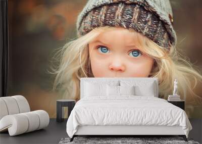 Young blonde girl wearing a blue jacket and a hat. She has blue eyes and a smile on her face Wall mural