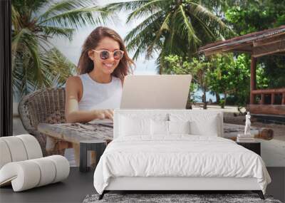 Young woman working with laptop computer on tropical island beach under palm trees Freelance  concept Wall mural