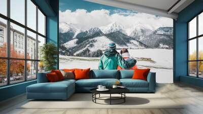 Back view photo of young loving couple hugging over winter mountains. Looking at mountains. Wall mural