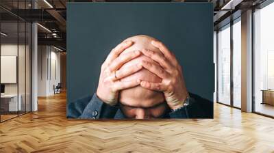 Frustrated bald man holding his head facing camera. Isolated on dark background Wall mural