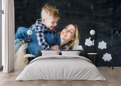 Portrait of loving young mother playing with her kid. Playful woman holding little cute son above her head. Wall mural