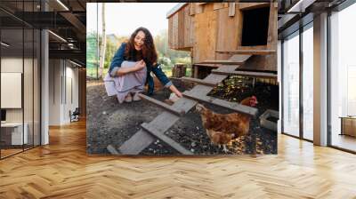 Joyful woman in chicken coop enjoying farm life by feeding chickens. Smiling farmer caring for her bird in her backyard in a rustic style, demonstrating an eco-friendly lifestyle Wall mural