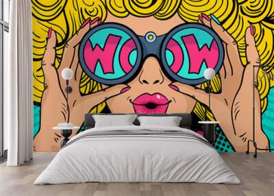 wow pop art face. sexy surprised woman with blonde curly hair and open mouth holding binoculars in h Wall mural