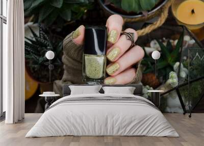 Closeup of woman's hand holding nail polish bottle with healthy green succulent houseplant. Wall mural