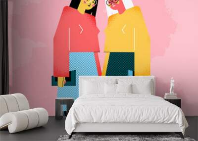 Two young women dressed in modern clothes are standing together. Meeting of friends or colleagues. Female geometric characters isolated on pink background Wall mural